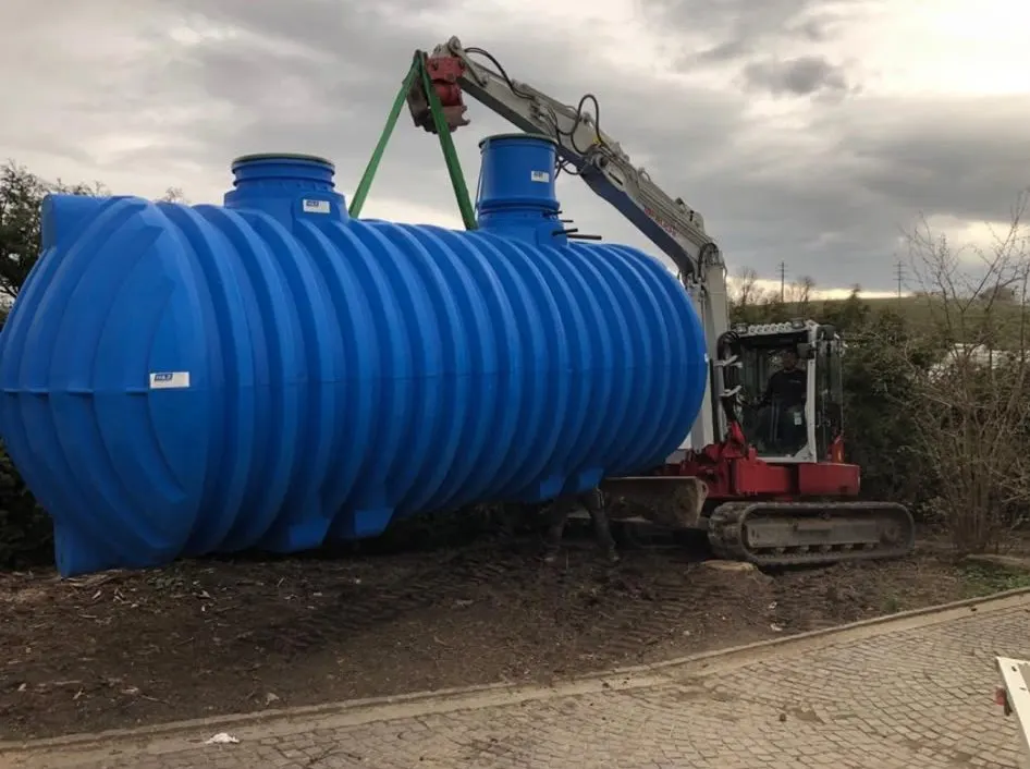 Grande citerne bleue de récupération d’eau de pluie levée par une pelle mécanique avant enfouissement