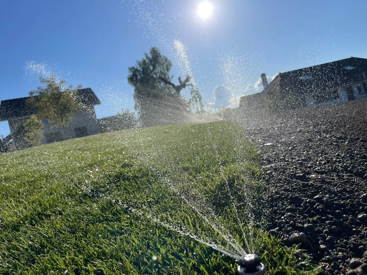 Arroseur escamotable en fonctionnement au bord d'une pelouse de villa, au soleil