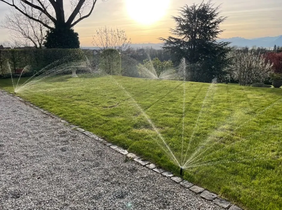 Arrosage automatique d’un jardin au coucher du soleil, jets d’eau à contre-jour