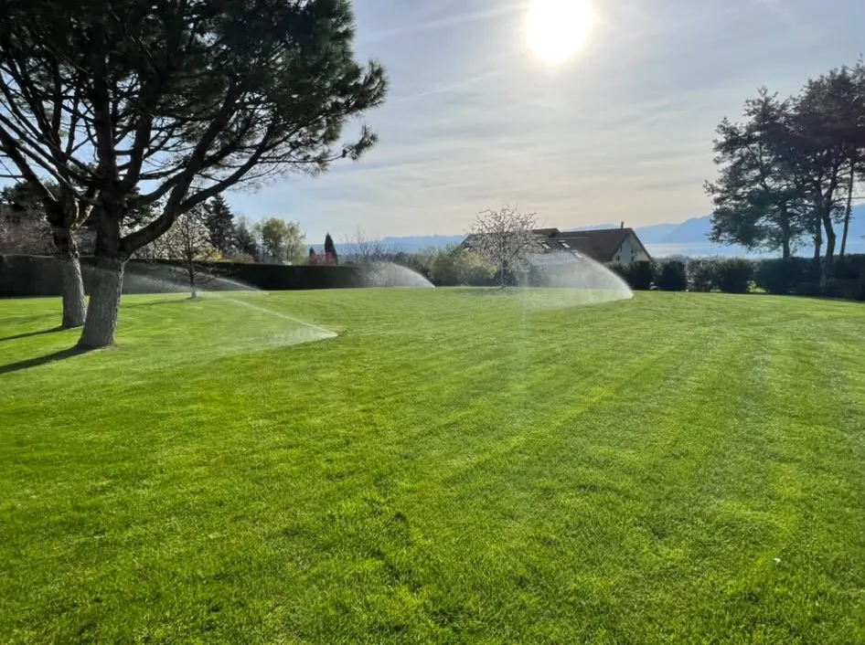 Grand jardin arboré arrosé par des arroseurs à turbine, pelouse et grands arbres