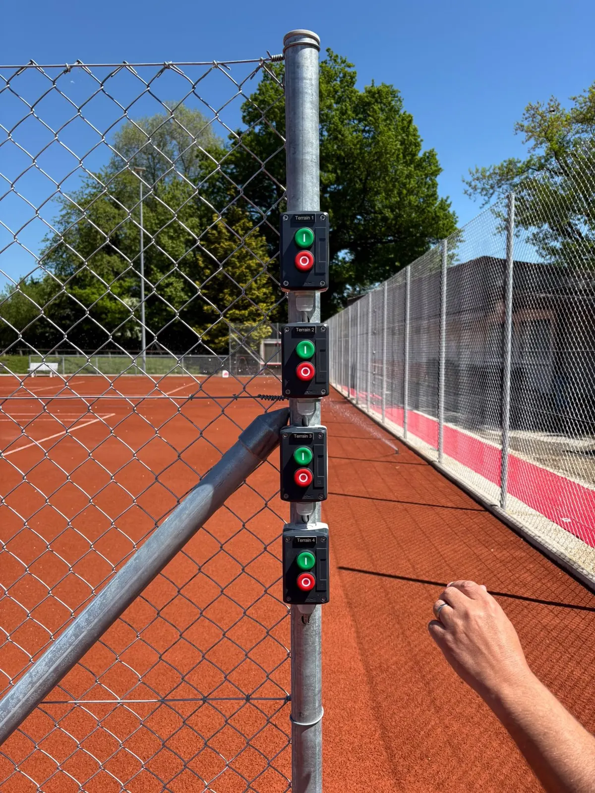 Programmateur d’arrosage fixé sur un poteau de clôture d’un court de tennis