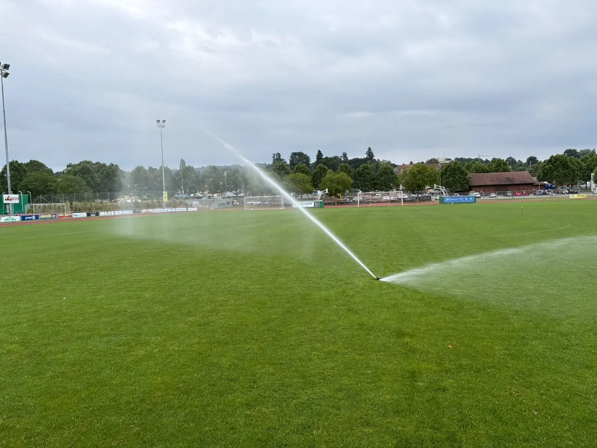 Arroseur à turbine en fonctionnement sur un terrain de football, ciel couvert