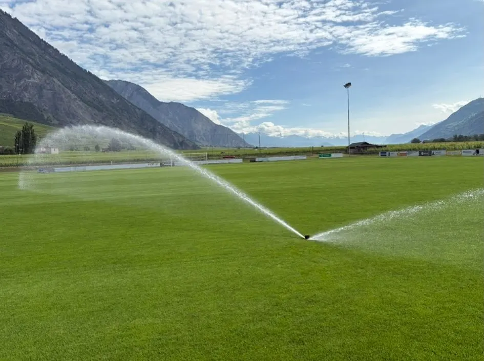 Terrain de football arrosé, montagnes en arrière-plan