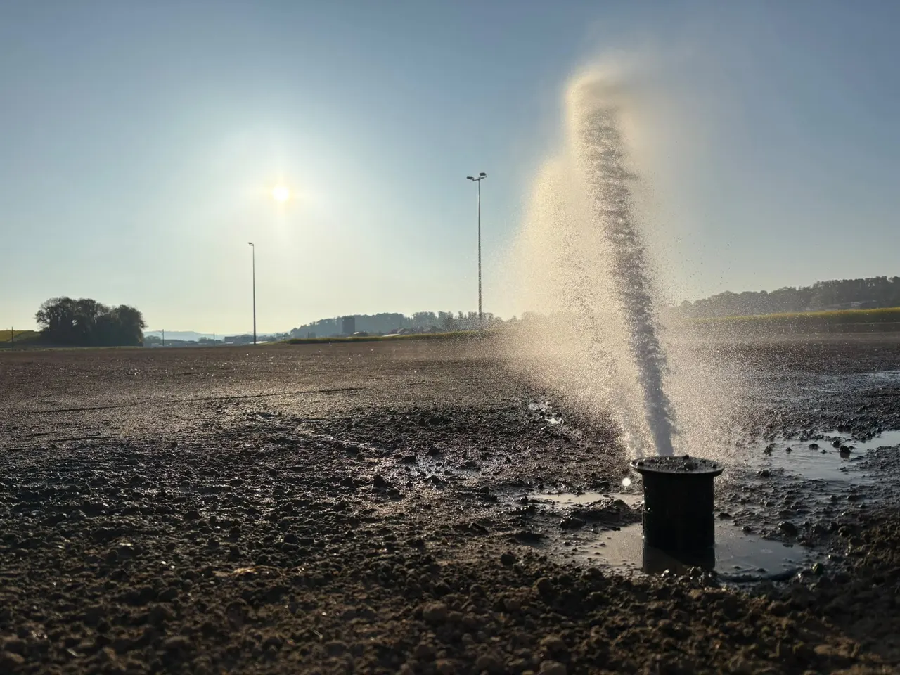 Mise en eau d'un arroseur sur un terrain de sport en construction au lever du soleil