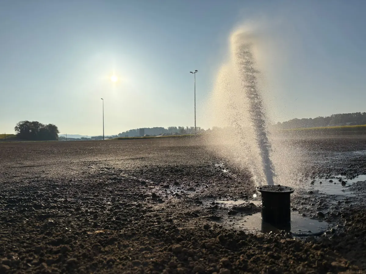 Mise en eau d’un arroseur sur un terrain de sport en construction, au lever du soleil