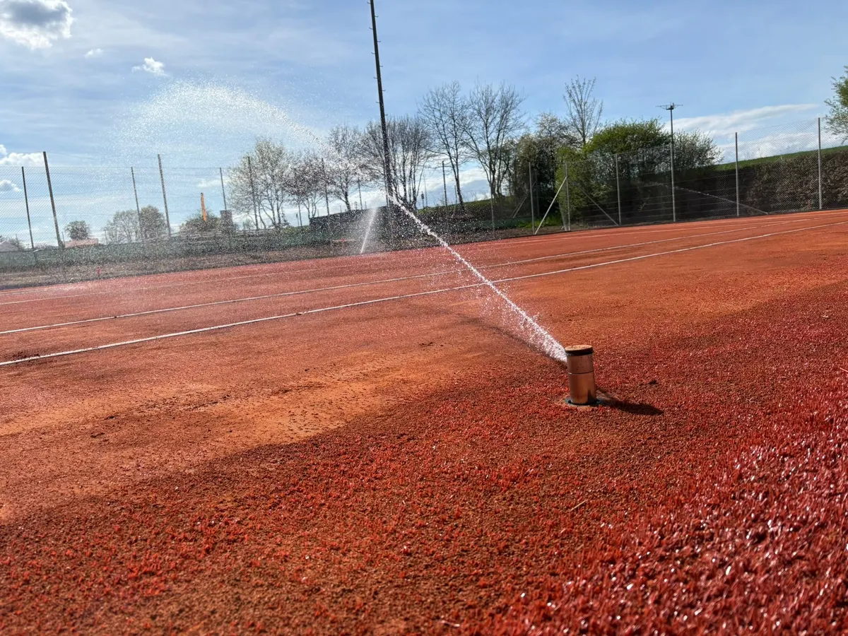 Arroseur escamotable sorti de terre sur un court de tennis en terre battue
