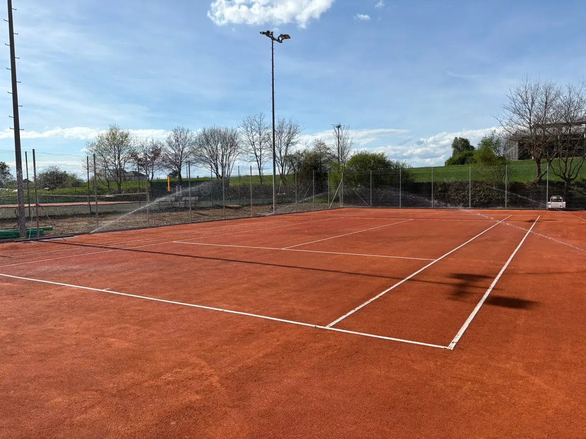 Court de tennis en terre battue arrosé par des arroseurs escamotables en périphérie